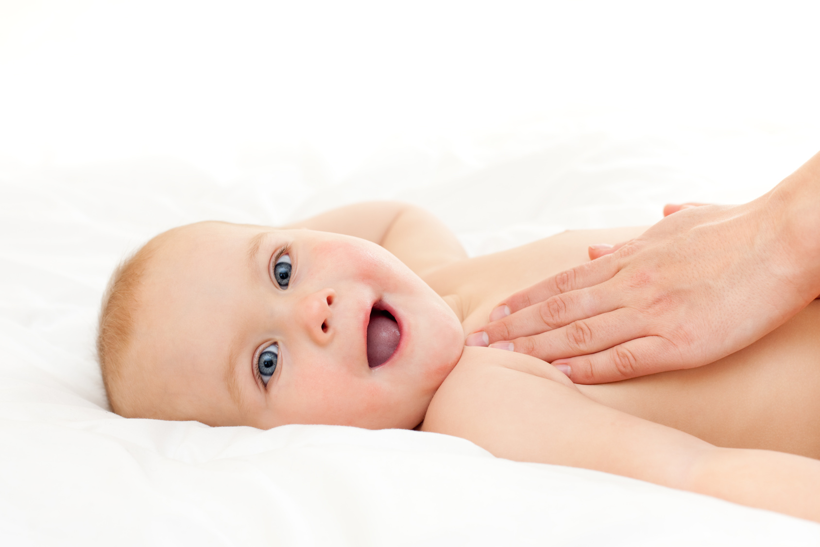Lachendes Baby Ein lächelndes Baby ruht auf einem Bett, während eine Hand es zärtlich hält.