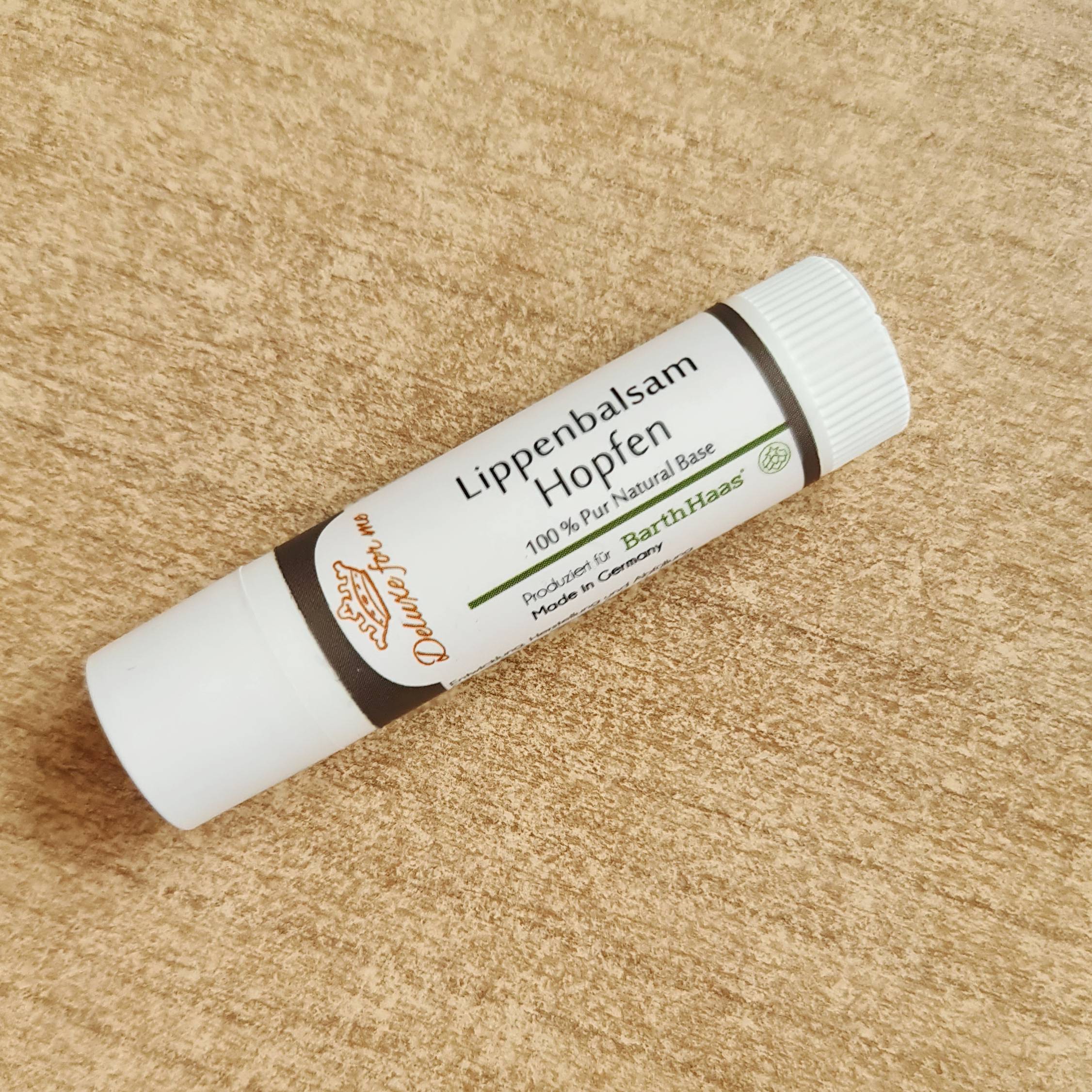 Lippenbalsam Hopfen Hier liegt ein Lippenpflegestift auf einem Tisch. Er trägt den Aufdruck Lippenbalsam Hopfen.